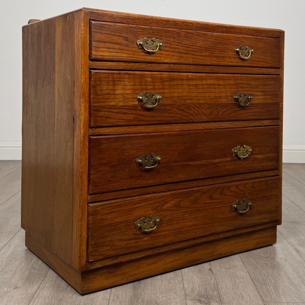 An antique golden oak chest of four drawers fitted with decorative brass drop handles on a plinth base. View VIII