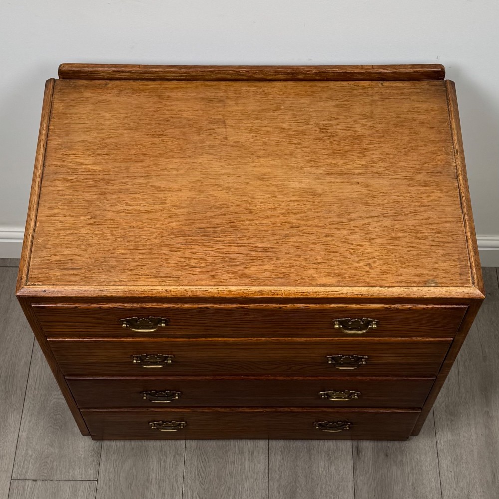 An antique golden oak chest of four drawers fitted with decorative brass drop handles on a plinth base. View IX