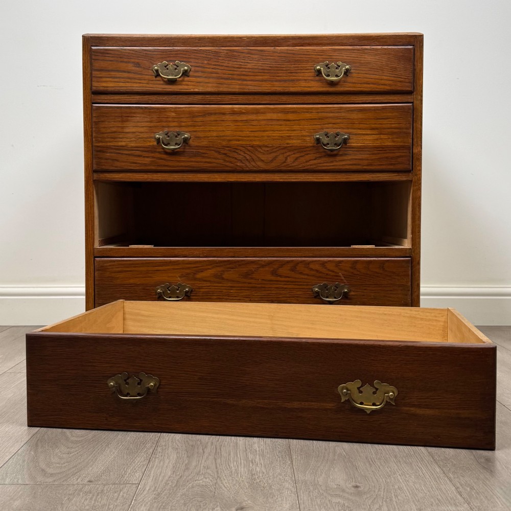 An antique golden oak chest of four drawers fitted with decorative brass drop handles on a plinth base. View X