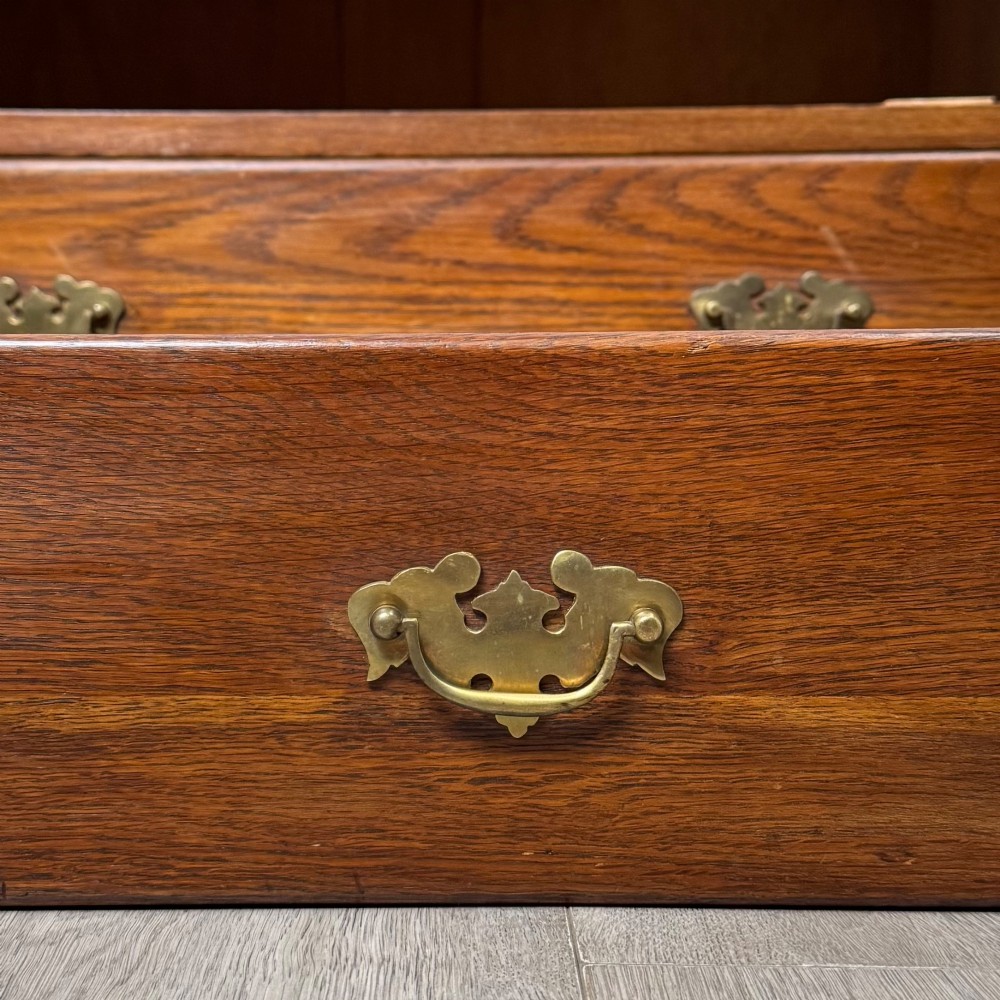 An antique golden oak chest of four drawers fitted with decorative brass drop handles on a plinth base. View XI
