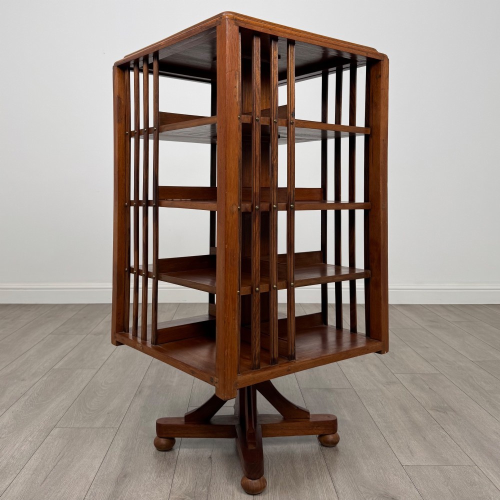 An Edwardian oak revolving bookcase with three tier shelves, open vertical slatted sides, and a central rotating column mounted on a quadruped base with castors. View VI