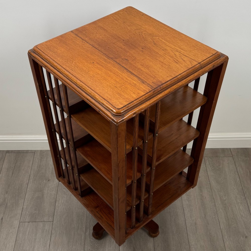 An Edwardian oak revolving bookcase with three tier shelves, open vertical slatted sides, and a central rotating column mounted on a quadruped base with castors. View VIII