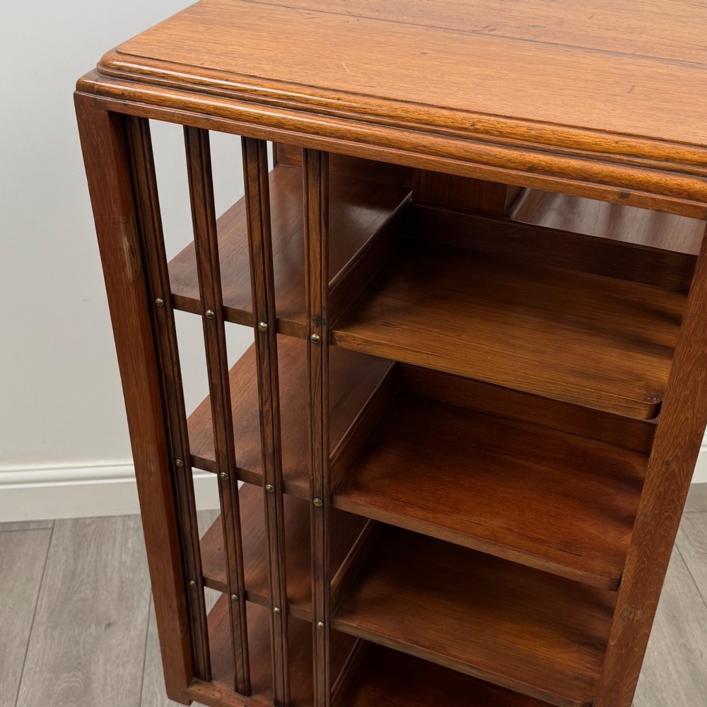 An Edwardian oak revolving bookcase with three tier shelves, open vertical slatted sides, and a central rotating column mounted on a quadruped base with castors. View IX