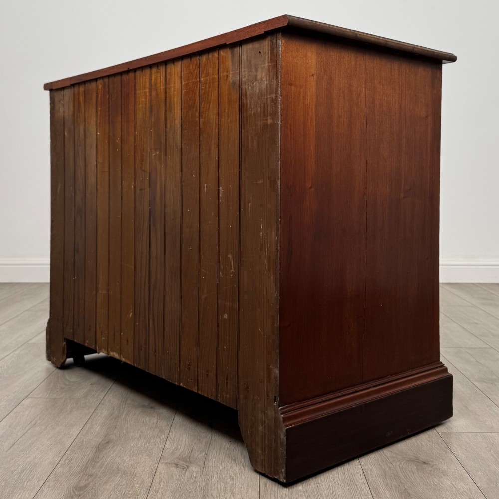 An antique mahogany chest of drawers featuring two short top drawers over two long lower drawers with decorative metal handles on a plinth base. View VI