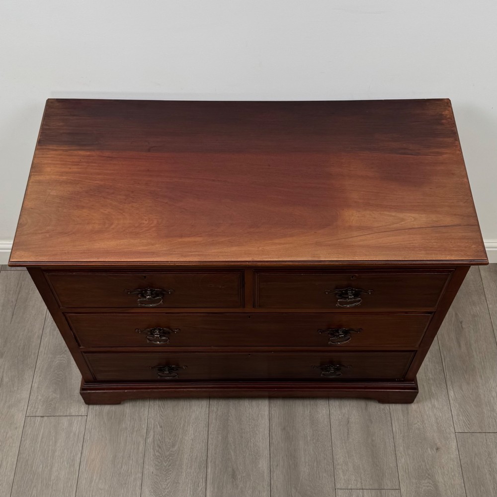 An antique mahogany chest of drawers featuring two short top drawers over two long lower drawers with decorative metal handles on a plinth base. View IX