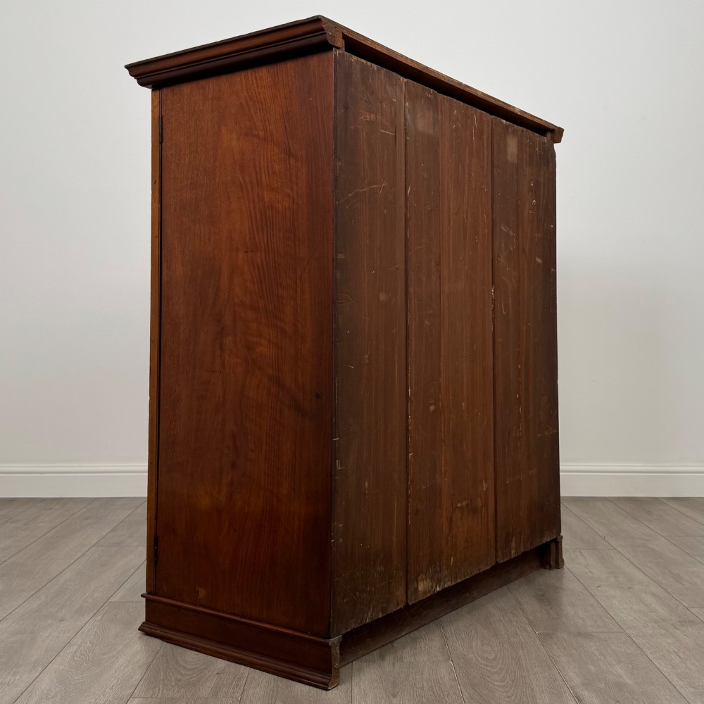 An antique early twentieth-century two-door walnut linen cupboard featuring double panelled doors, a moulded top cornice, and a central brass teardrop handle. View V