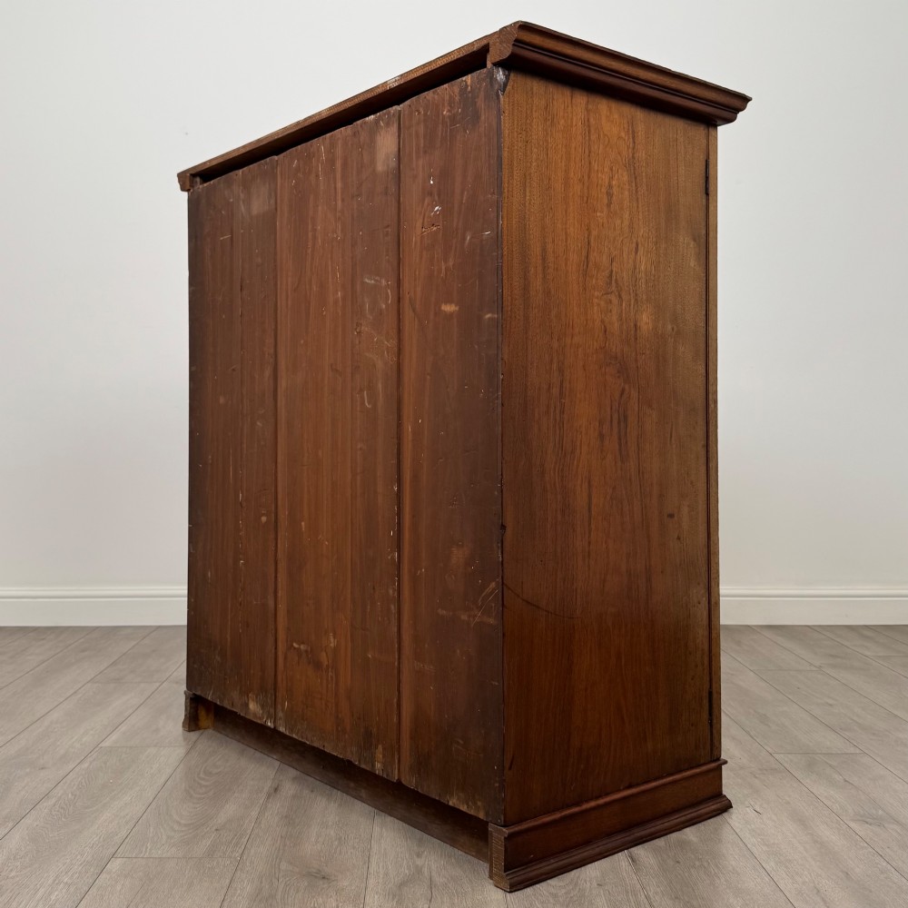 An antique early twentieth-century two-door walnut linen cupboard featuring double panelled doors, a moulded top cornice, and a central brass teardrop handle. View VII