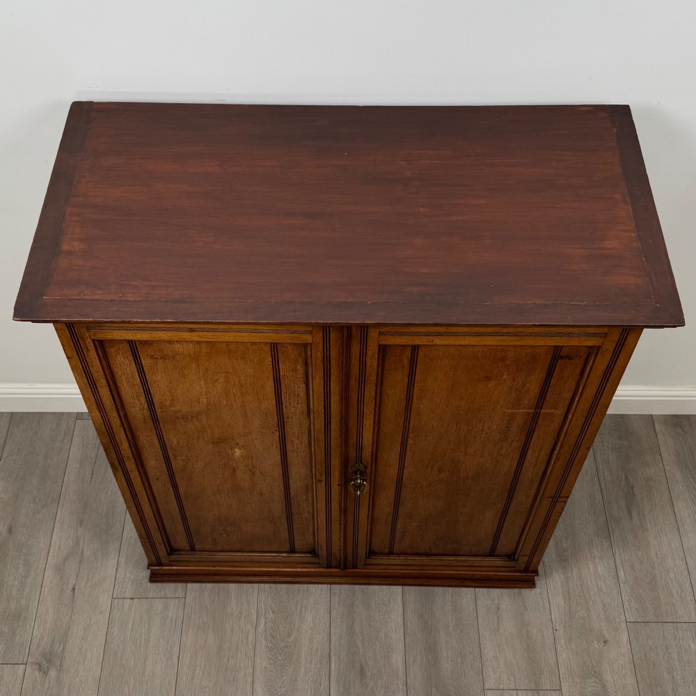 An antique early twentieth-century two-door walnut linen cupboard featuring double panelled doors, a moulded top cornice, and a central brass teardrop handle. View X