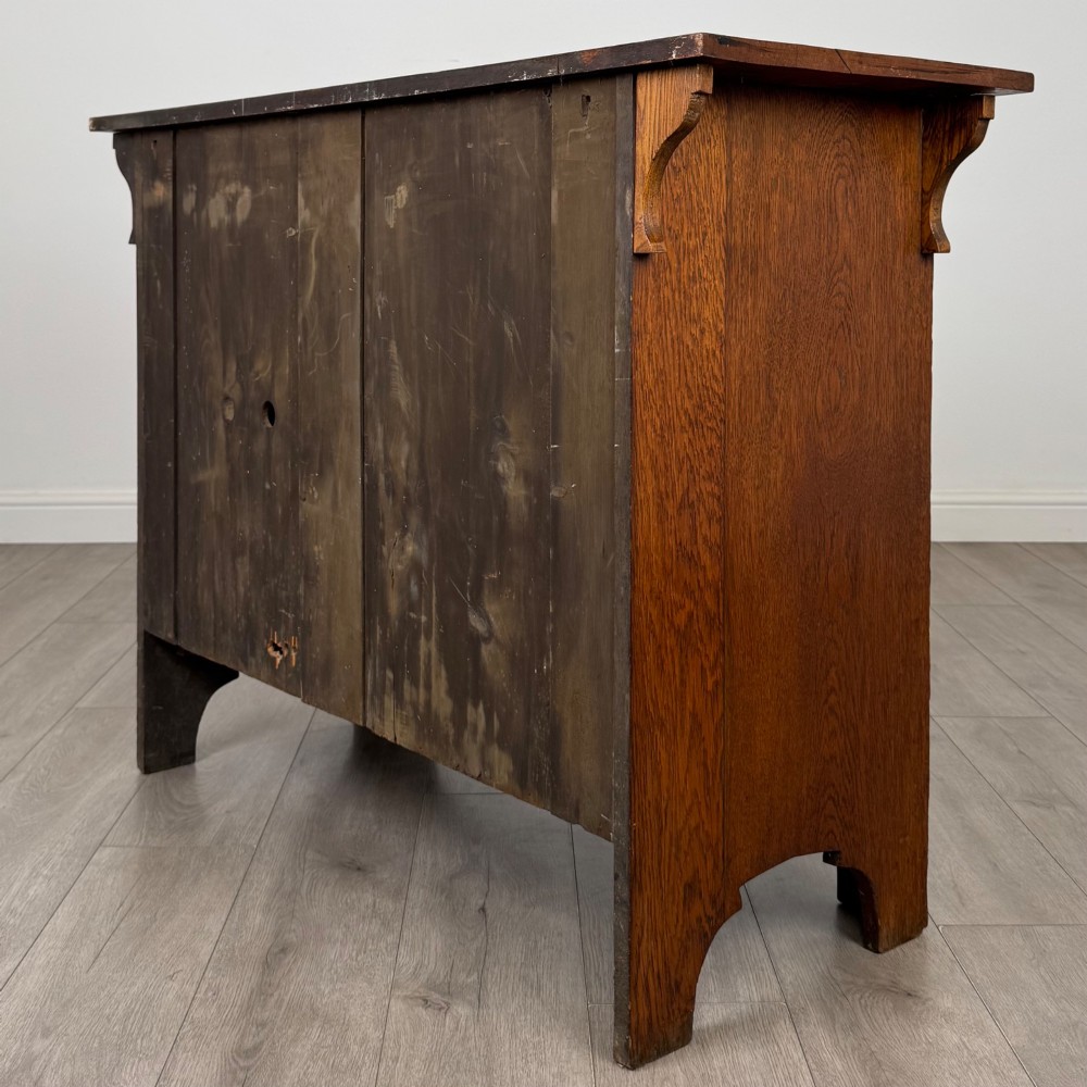 An Arts and Crafts golden oak sideboard featuring two top drawers, two lower cupboard doors, and stylized copper strap hinges. View VII