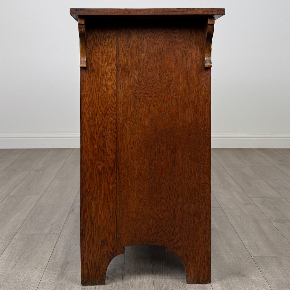 An Arts and Crafts golden oak sideboard featuring two top drawers, two lower cupboard doors, and stylized copper strap hinges. View VIII