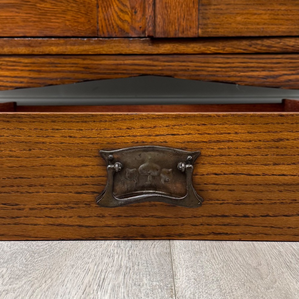 An Arts and Crafts golden oak sideboard featuring two top drawers, two lower cupboard doors, and stylized copper strap hinges. View XII