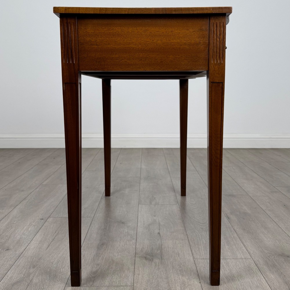 A 20th-century burr walnut side table featuring a serpentine front, three drawer fronts with brass handles, and square tapered legs. View VII