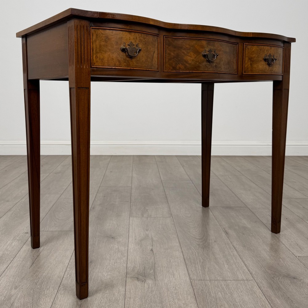 A 20th-century burr walnut side table featuring a serpentine front, three drawer fronts with brass handles, and square tapered legs. View VIII