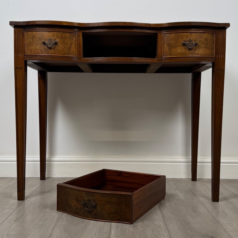 A 20th-century burr walnut side table featuring a serpentine front, three drawer fronts with brass handles, and square tapered legs. View X