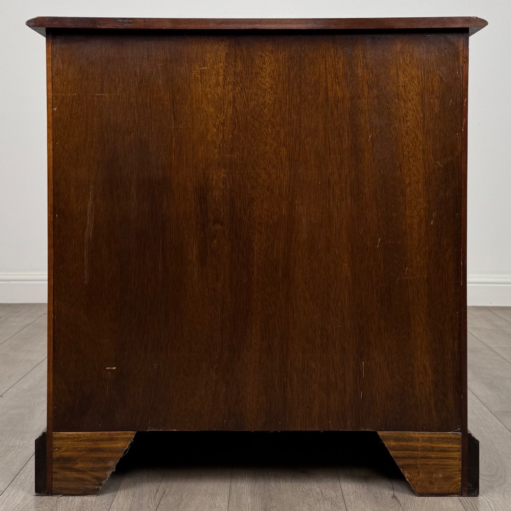 A 20th-century serpentine-front hardwood chest featuring four stacked drawers with brass drop ring handles and central brass escutcheons. View V