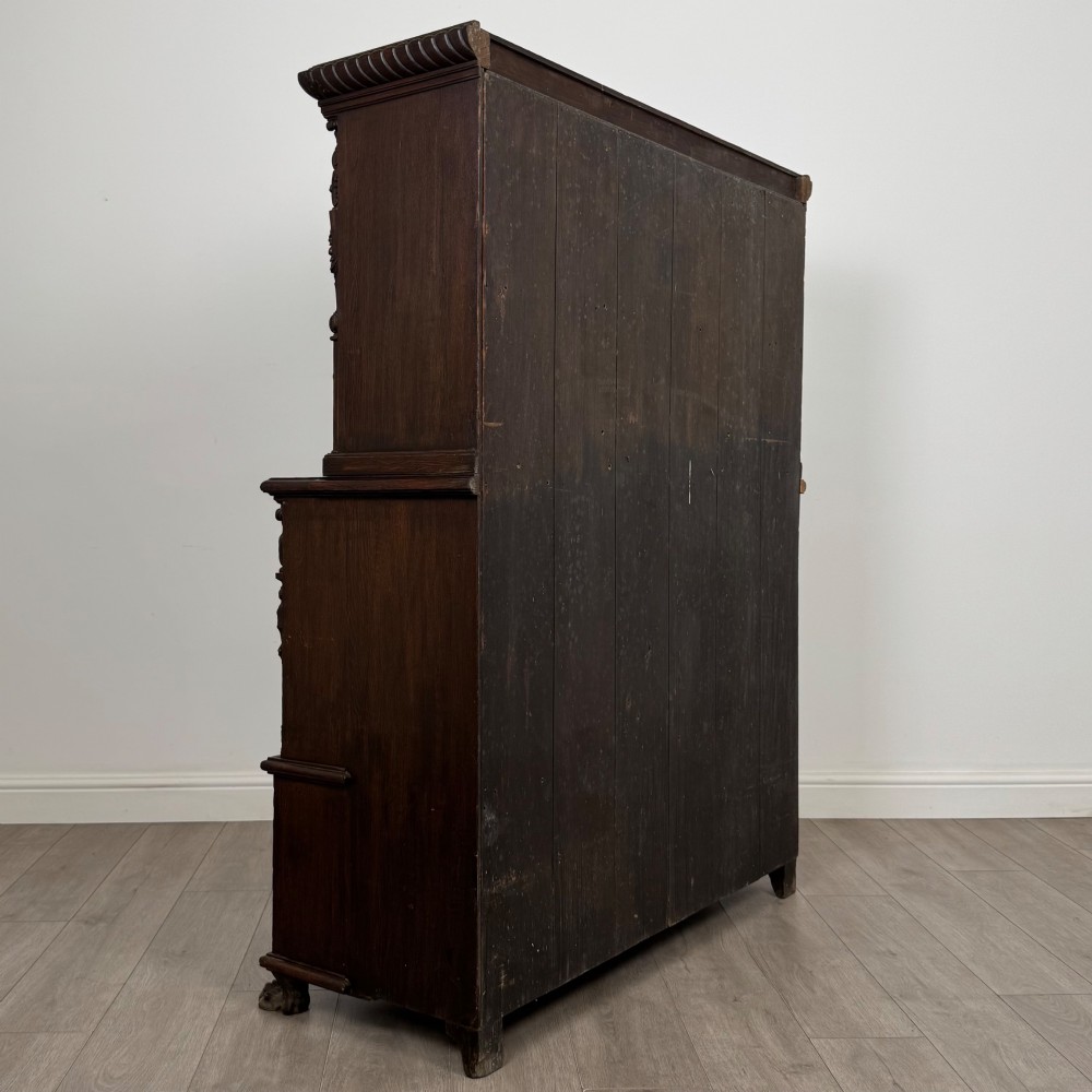 A 19th-century dark oak carved cupboard featuring an open top shelf, carved lion cresting, relief-carved panel doors with figures, and an open lower base. View V