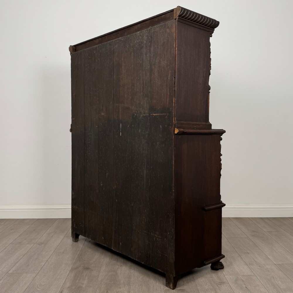A 19th-century dark oak carved cupboard featuring an open top shelf, carved lion cresting, relief-carved panel doors with figures, and an open lower base. View VII
