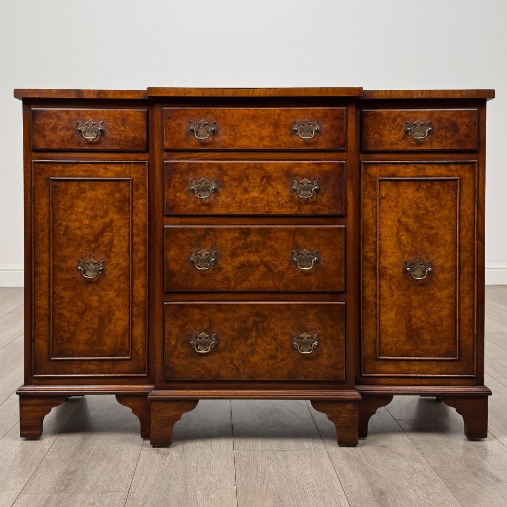 An antique 20th-century small breakfront sideboard with figured burr walnut veneers, brass drop handles, four central drawers, and side cupboard doors.