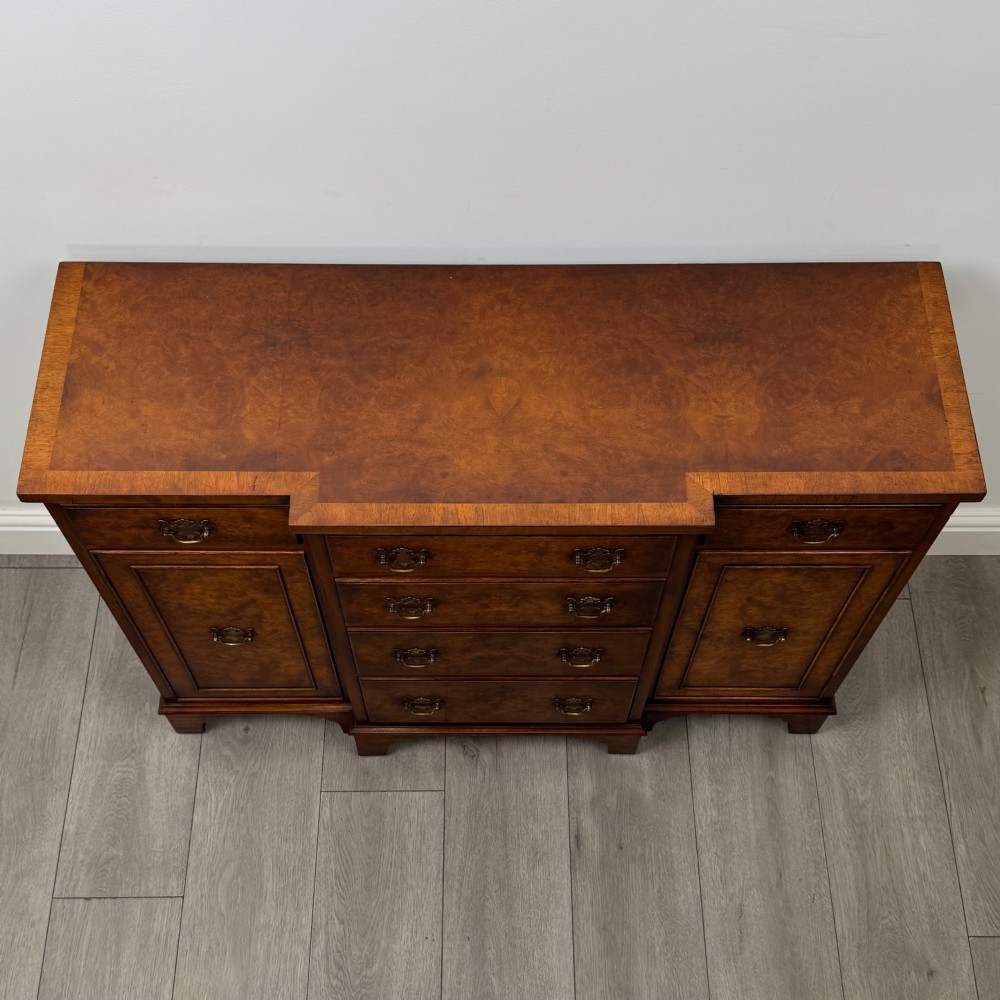 An antique 20th-century small breakfront sideboard with figured burr walnut veneers, brass drop handles, four central drawers, and side cupboard doors. View X