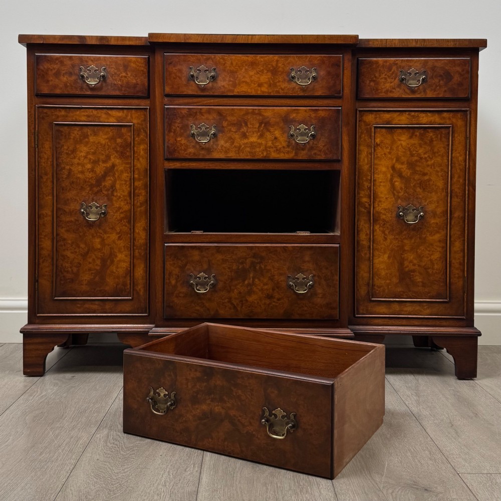 An antique 20th-century small breakfront sideboard with figured burr walnut veneers, brass drop handles, four central drawers, and side cupboard doors. View XI
