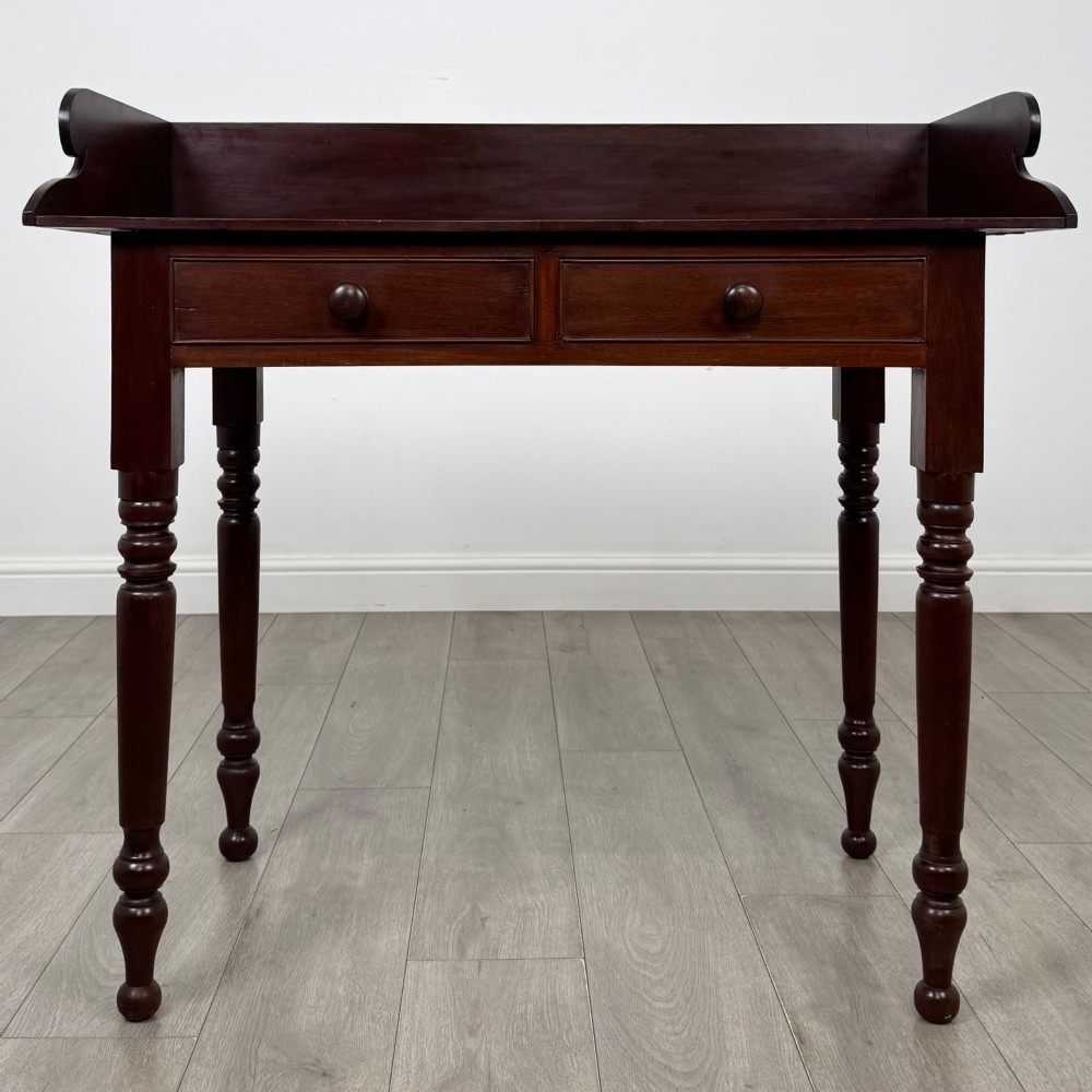 A 19th-century dark mahogany writing table featuring a raised gallery back upstand, two frieze drawers with turned handles, and four turned legs.