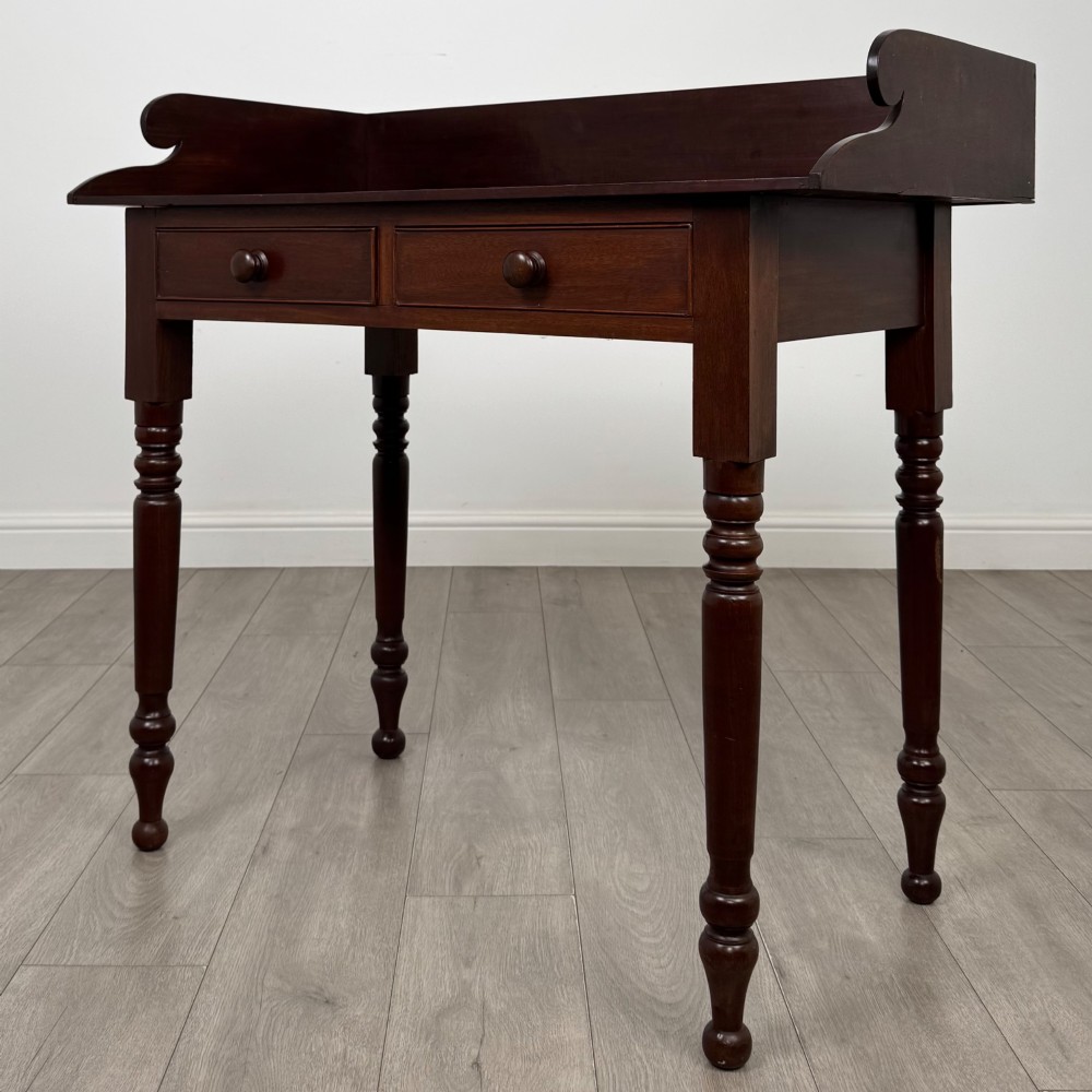 A 19th-century dark mahogany writing table featuring a raised gallery back upstand, two frieze drawers with turned handles, and four turned legs. View II