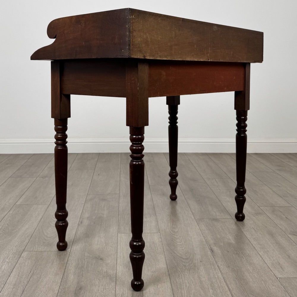 A 19th-century dark mahogany writing table featuring a raised gallery back upstand, two frieze drawers with turned handles, and four turned legs. View IV
