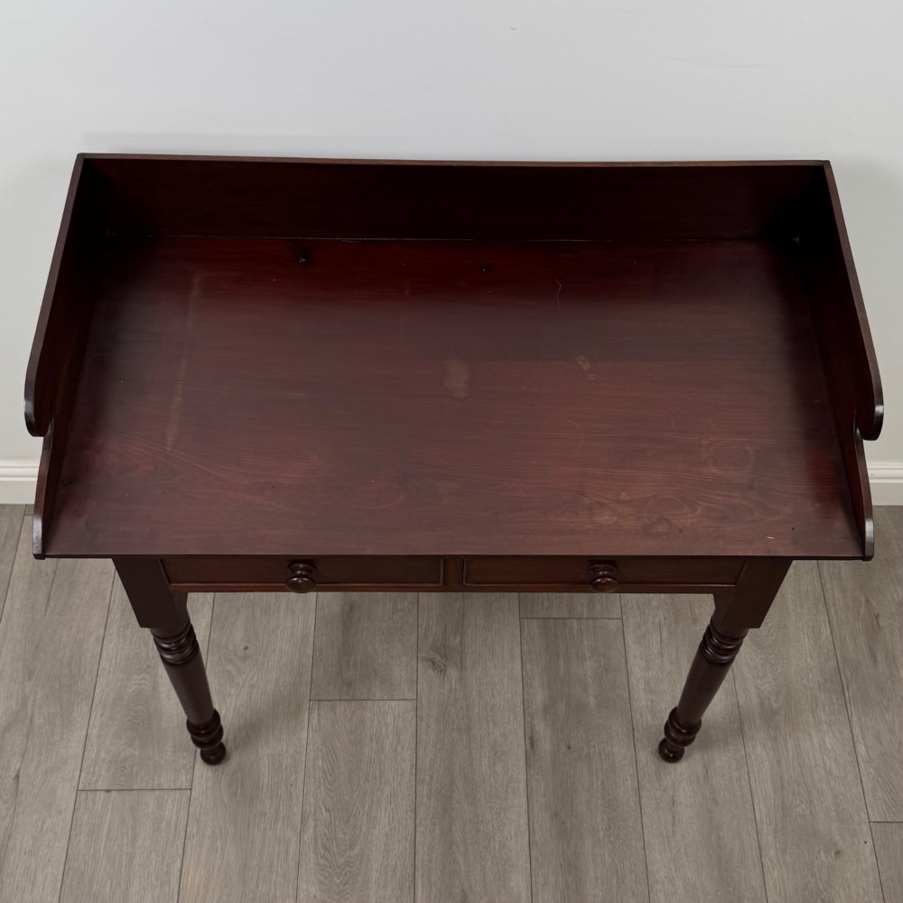 A 19th-century dark mahogany writing table featuring a raised gallery back upstand, two frieze drawers with turned handles, and four turned legs. View IX