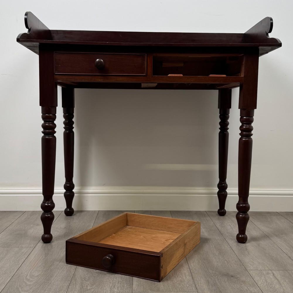 A 19th-century dark mahogany writing table featuring a raised gallery back upstand, two frieze drawers with turned handles, and four turned legs. View X