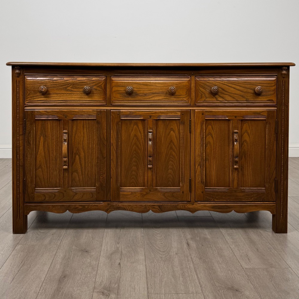 A warm brown solid oak sideboard with three drawers positioned above three fielded panel cupboard doors.
