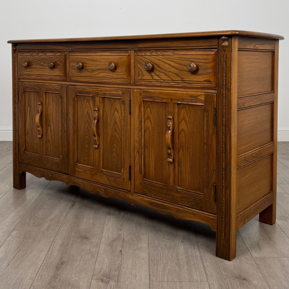 A warm brown solid oak sideboard with three drawers positioned above three fielded panel cupboard doors. View III