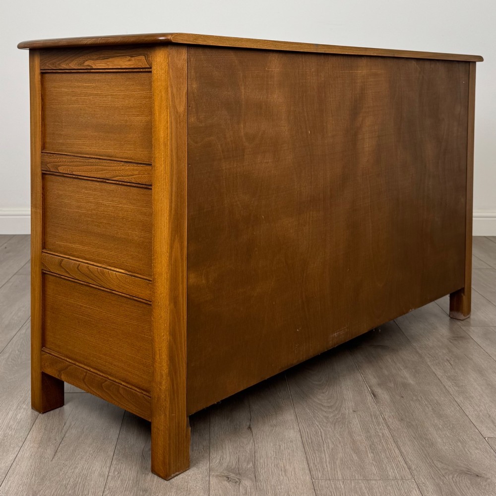 A warm brown solid oak sideboard with three drawers positioned above three fielded panel cupboard doors. View V