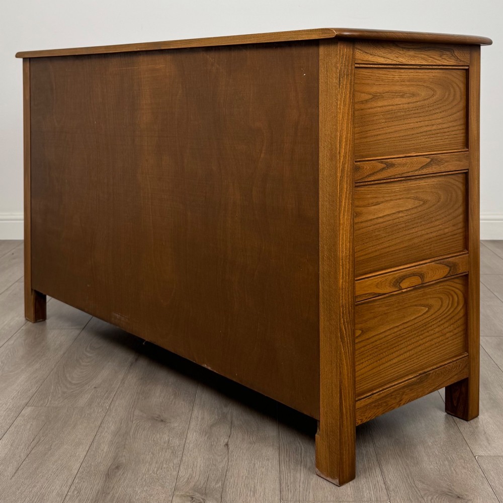 A warm brown solid oak sideboard with three drawers positioned above three fielded panel cupboard doors. View VII