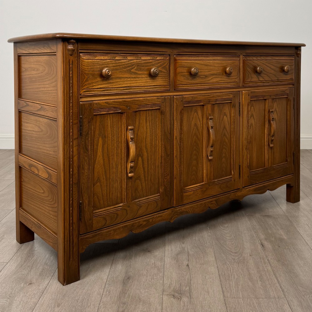 A warm brown solid oak sideboard with three drawers positioned above three fielded panel cupboard doors. View IX