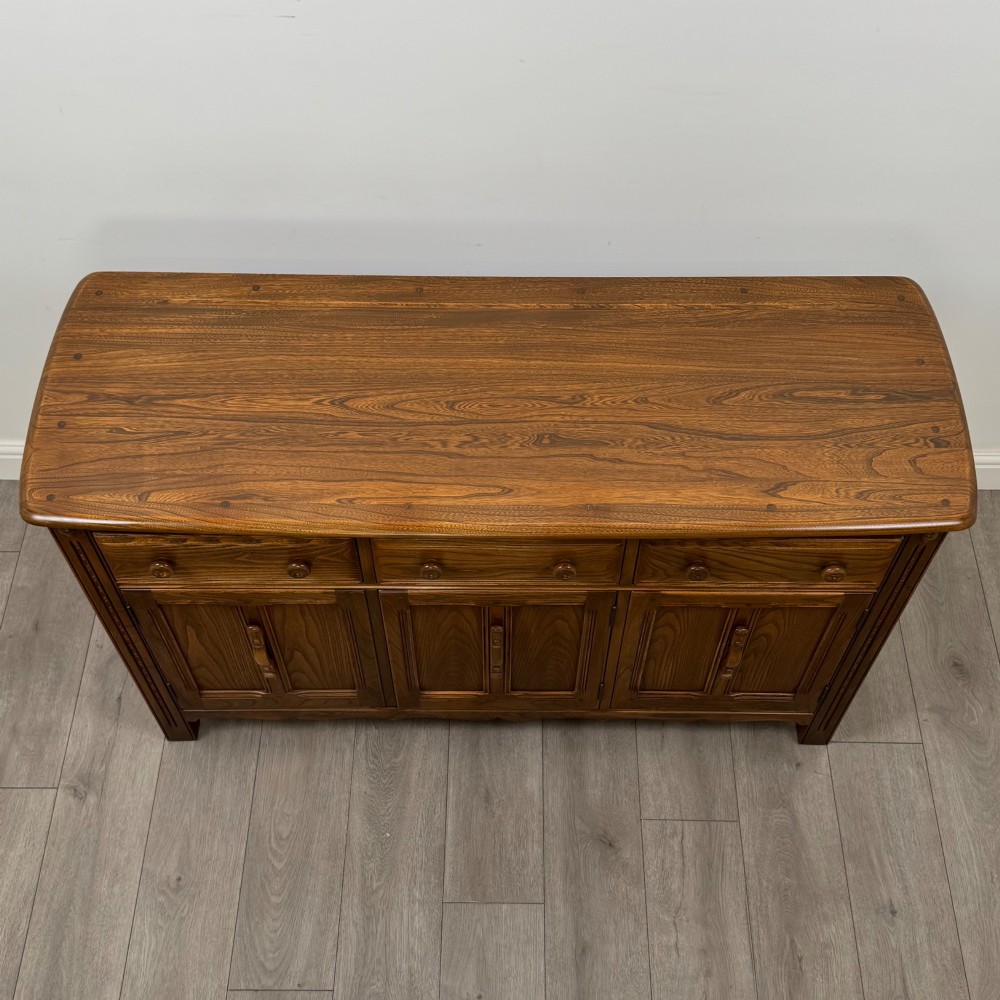 A warm brown solid oak sideboard with three drawers positioned above three fielded panel cupboard doors. View X