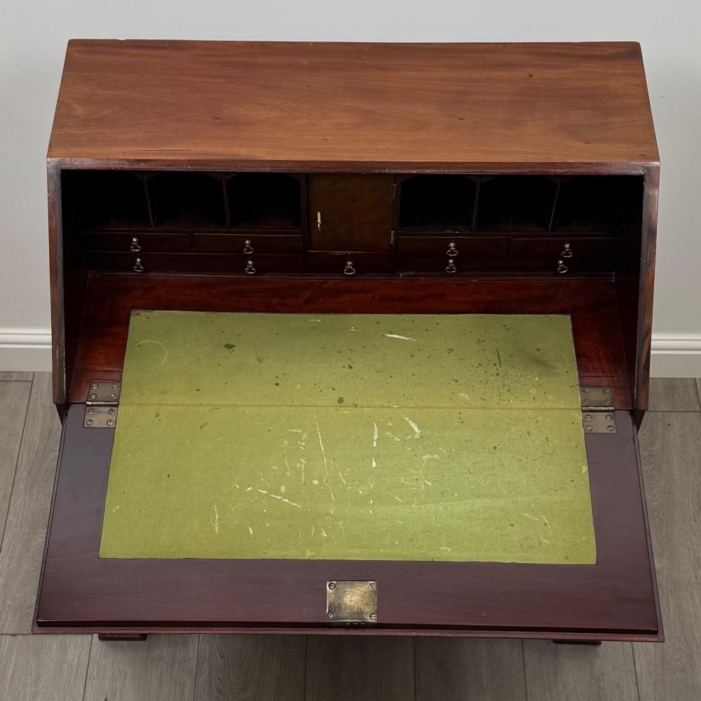 An 18th-century Georgian mahogany bureau featuring a sloped fall-front lid, brass batwing handles and escutcheons, three graduated drawers, and bracket feet. View XI