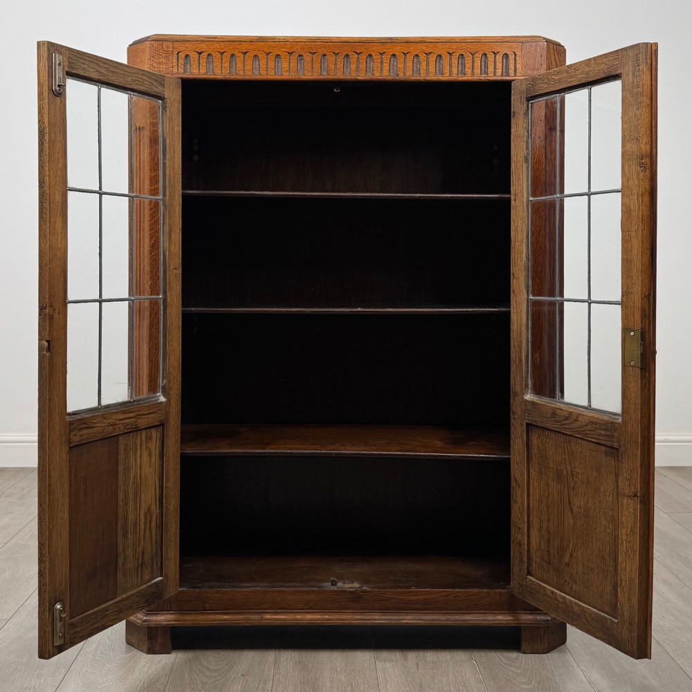 A twin-door dark oak display cabinet featuring leaded glass upper panels, carved decorative lower panels, and ornate metal hinges. View II