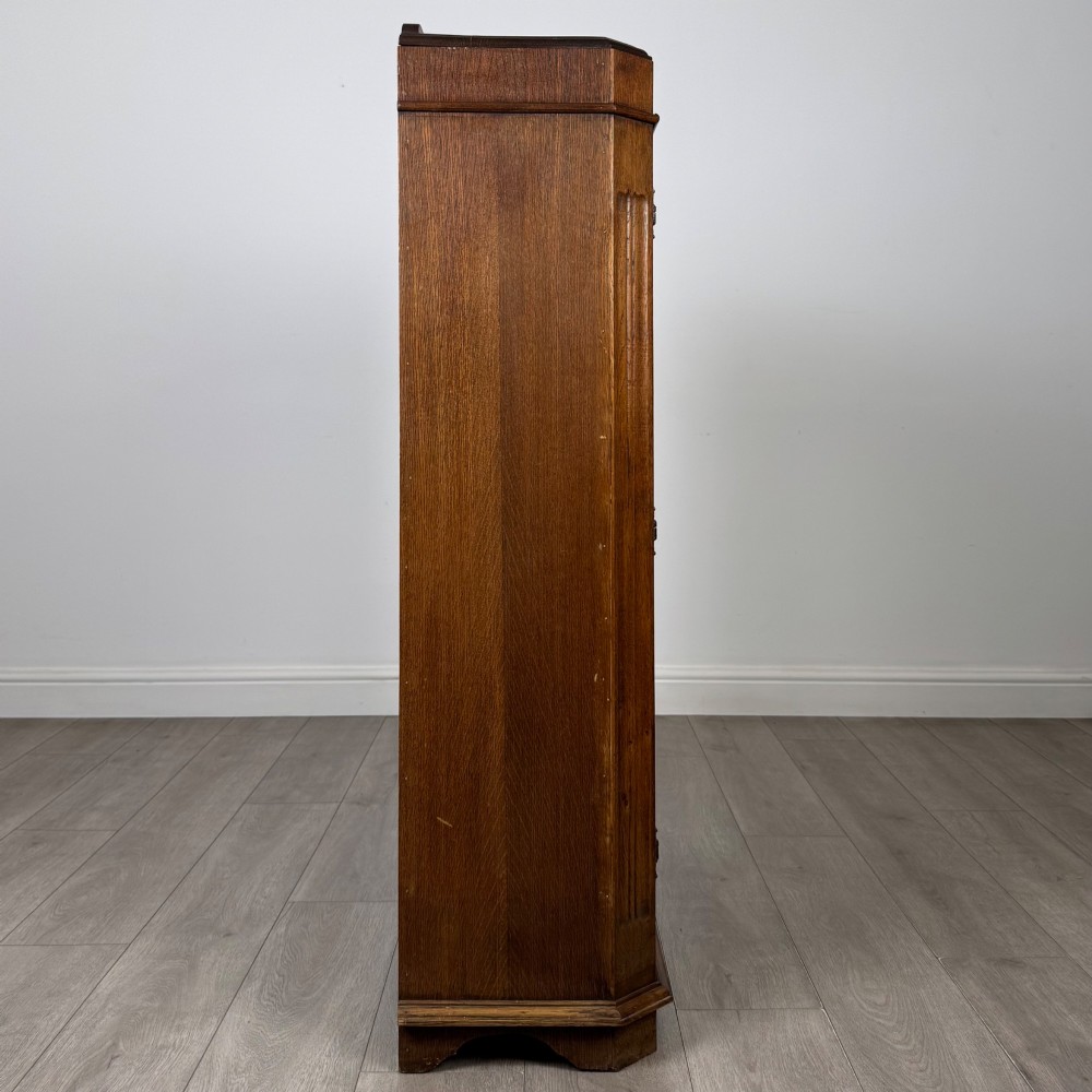 A twin-door dark oak display cabinet featuring leaded glass upper panels, carved decorative lower panels, and ornate metal hinges. View VIII