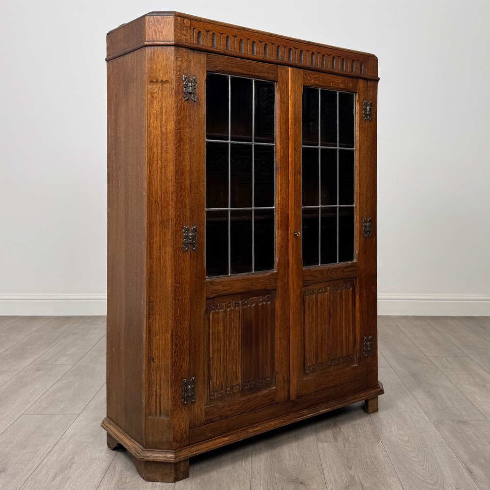 A twin-door dark oak display cabinet featuring leaded glass upper panels, carved decorative lower panels, and ornate metal hinges. View IX