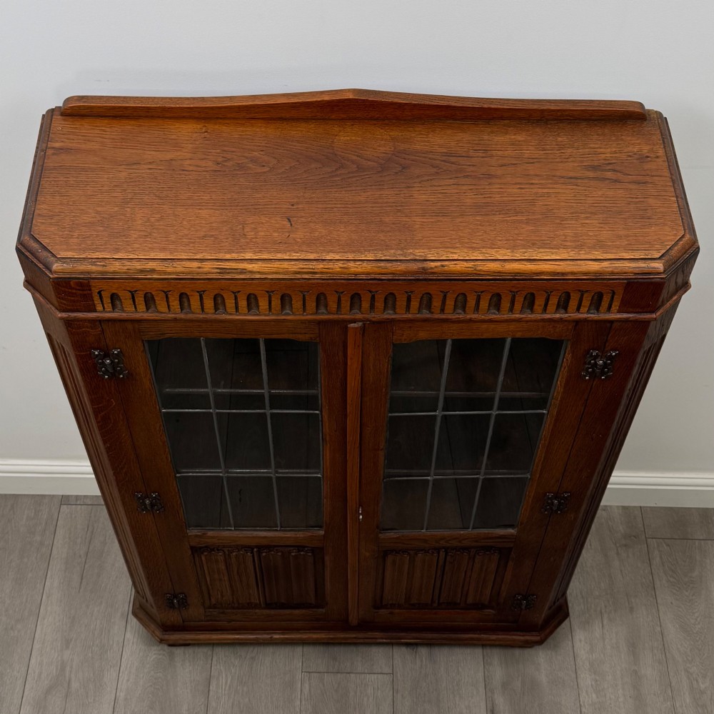 A twin-door dark oak display cabinet featuring leaded glass upper panels, carved decorative lower panels, and ornate metal hinges. View X