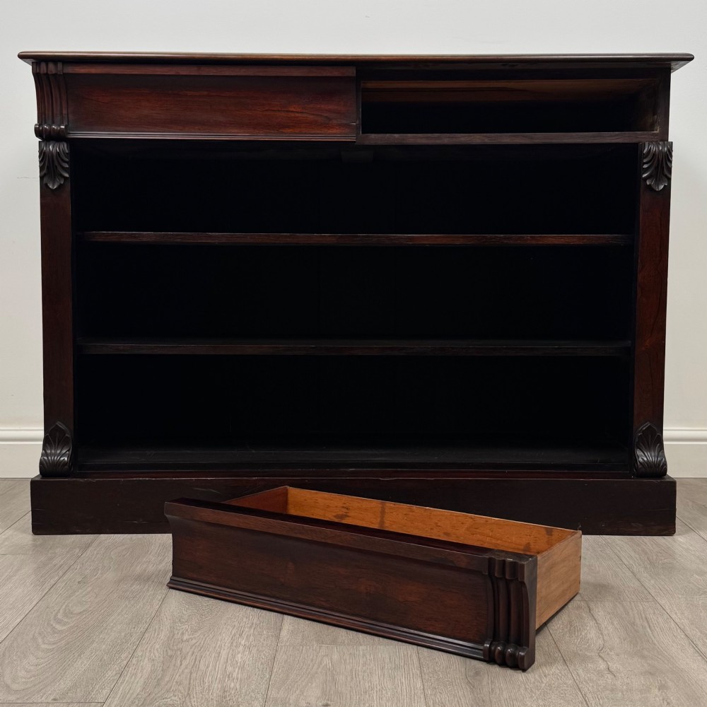 A low 19th-century Victorian rosewood open bookcase with two wide shelves, carved acanthus leaf capitals, and a solid plinth base. View X