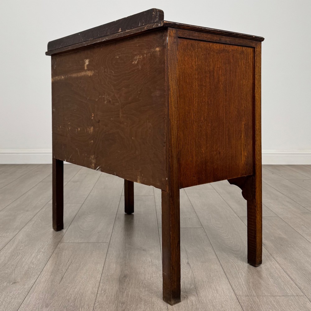 An antique golden oak chest of drawers featuring two wide drawers with stylised dark metal handles and a scalloped lower apron. View VI