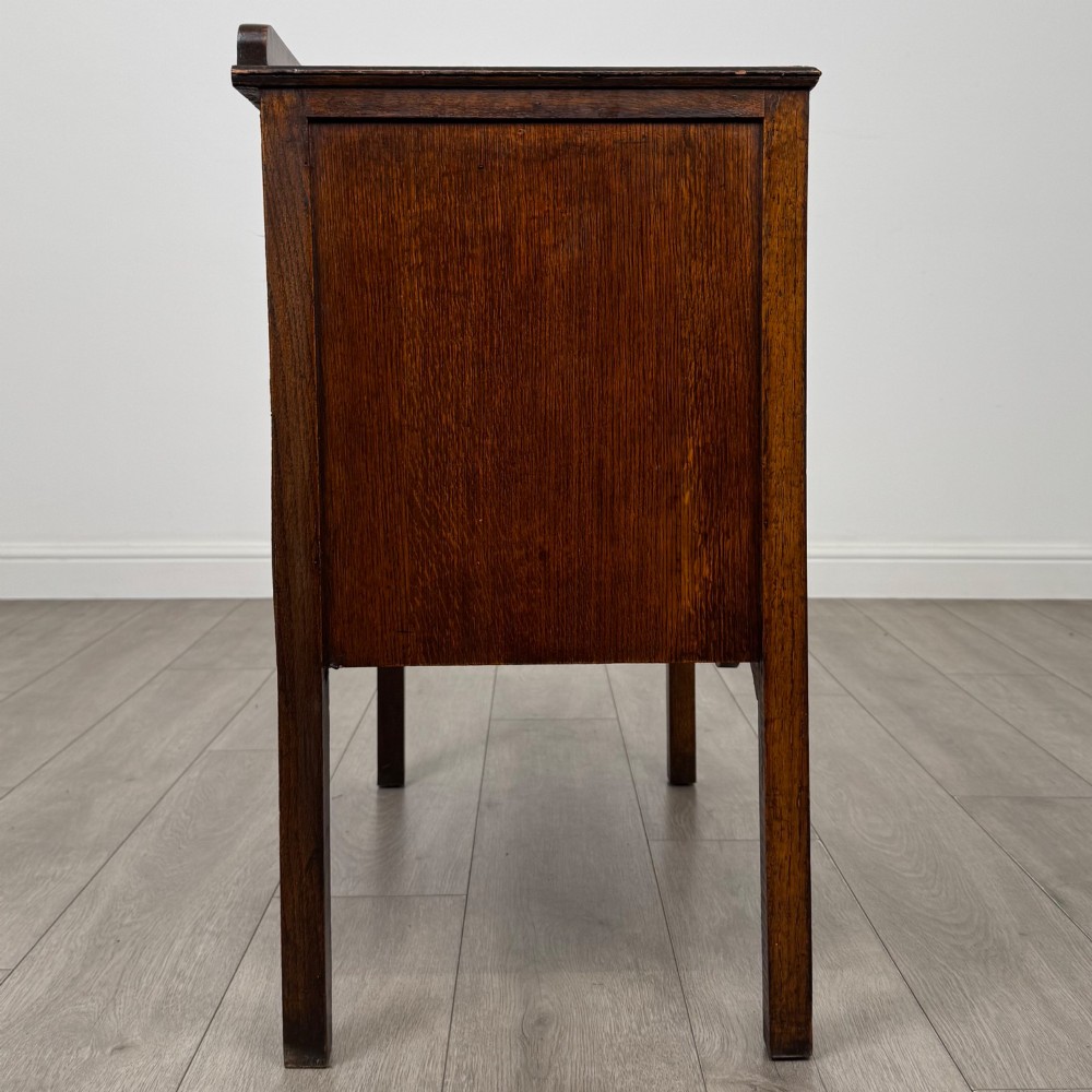 An antique golden oak chest of drawers featuring two wide drawers with stylised dark metal handles and a scalloped lower apron. View VII