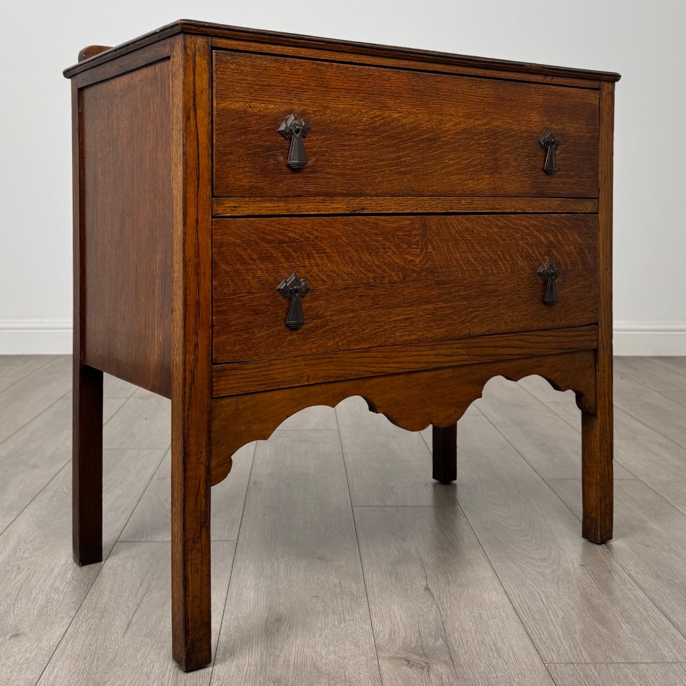 An antique golden oak chest of drawers featuring two wide drawers with stylised dark metal handles and a scalloped lower apron. View VIII