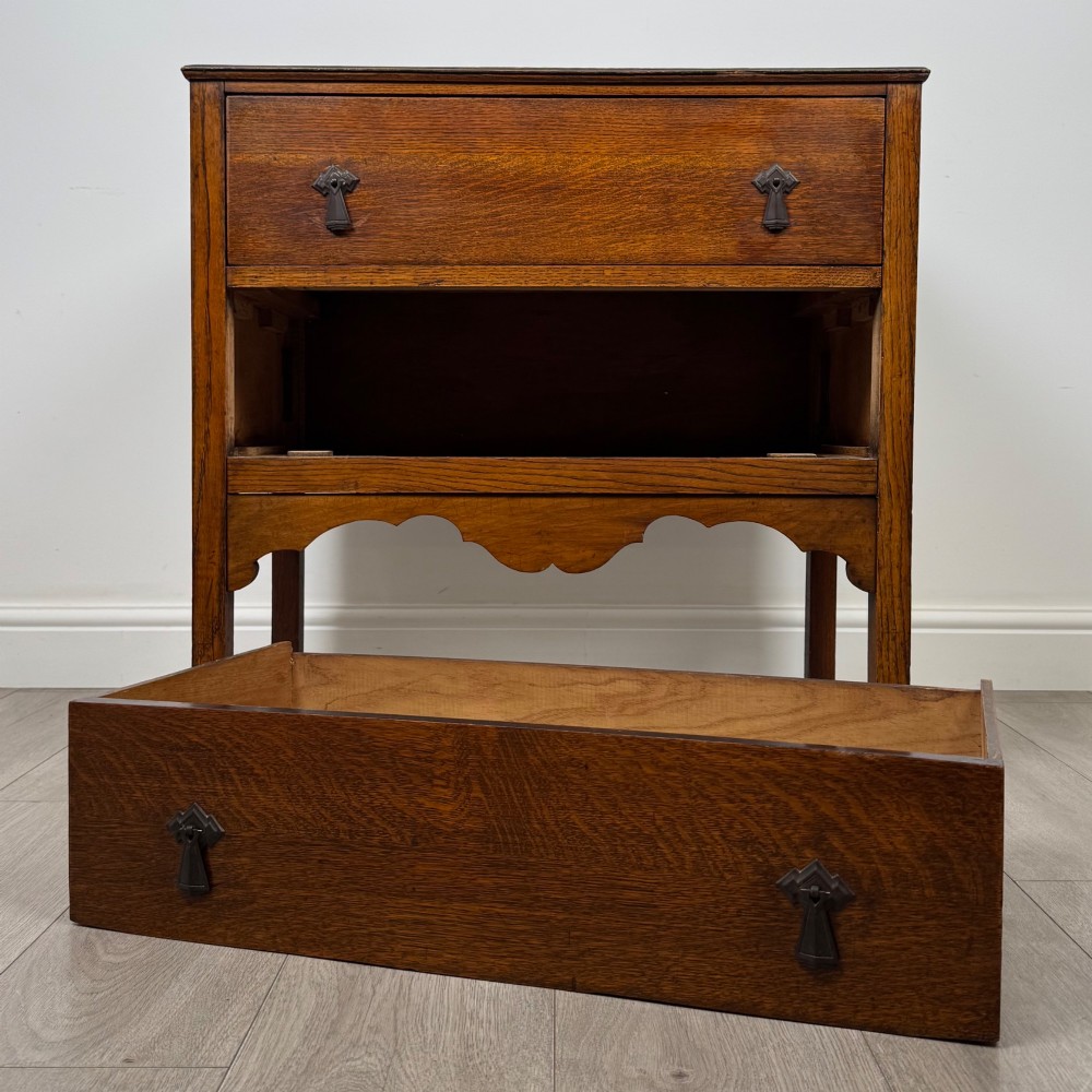 An antique golden oak chest of drawers featuring two wide drawers with stylised dark metal handles and a scalloped lower apron. View X