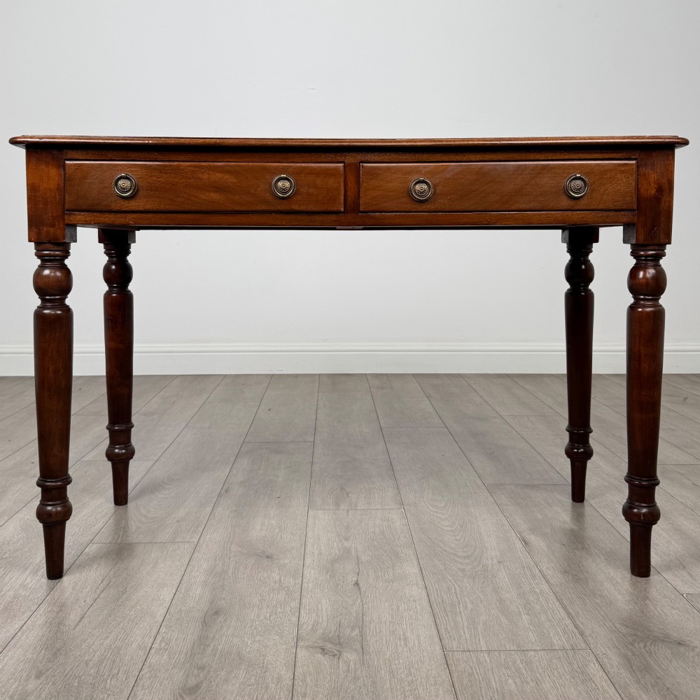 A Victorian mahogany writing table featuring two frieze drawers with brass ring handles and four turned legs.
