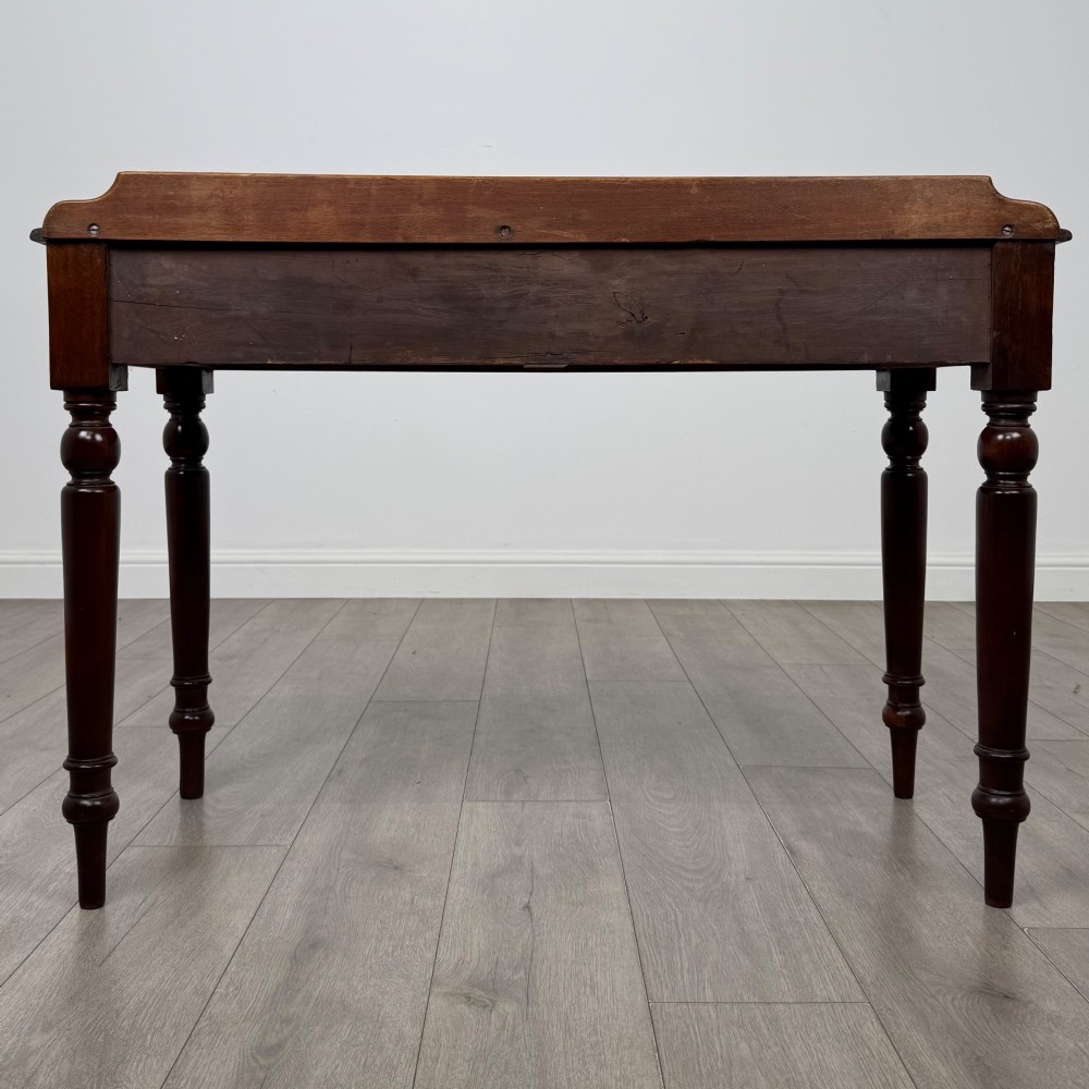 A Victorian mahogany writing table featuring two frieze drawers with brass ring handles and four turned legs. View V
