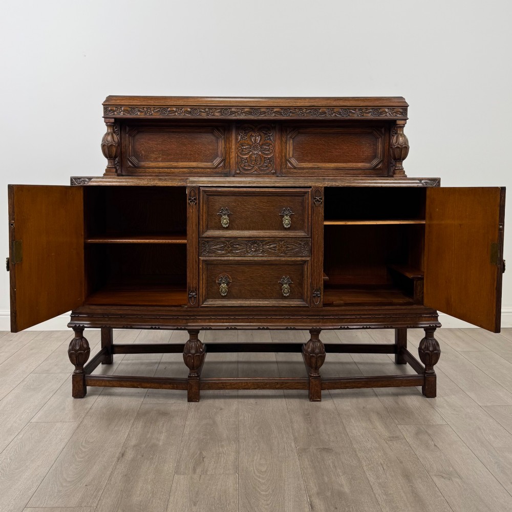 A dark carved oak sideboard featuring a raised gallery back, geometric octagonal panel doors, two central drawers with brass handles, and bulbous turned legs. View II