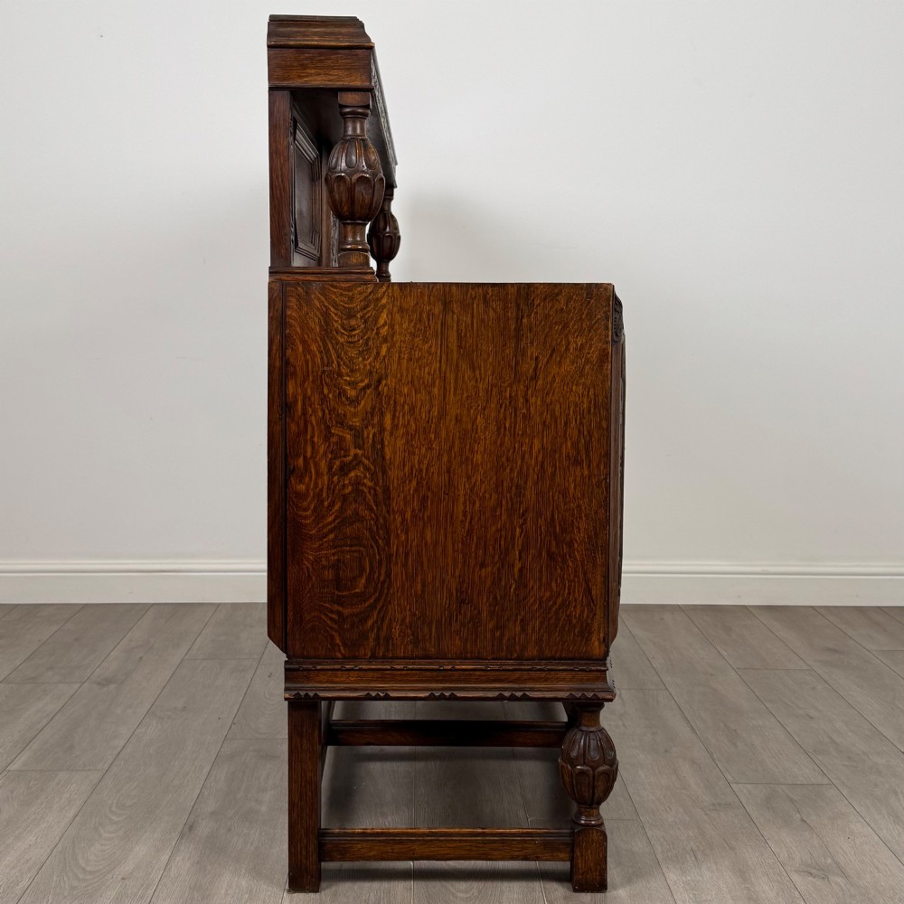 A dark carved oak sideboard featuring a raised gallery back, geometric octagonal panel doors, two central drawers with brass handles, and bulbous turned legs. View VIII