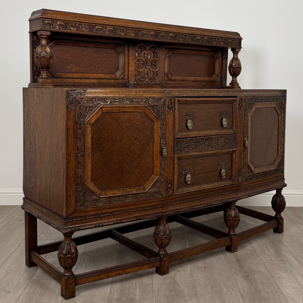 A dark carved oak sideboard featuring a raised gallery back, geometric octagonal panel doors, two central drawers with brass handles, and bulbous turned legs. View IX
